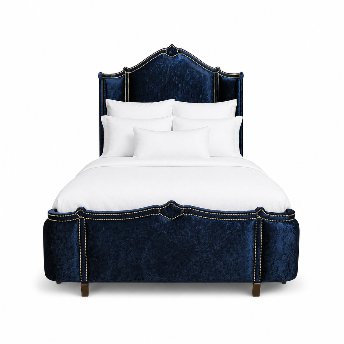 A luxury bed with a tall, curved headboard and matching footboard upholstered in deep navy blue crushed velvet, accented with antique gold nail head trim. All Haute House products are built in the United States and customizable 